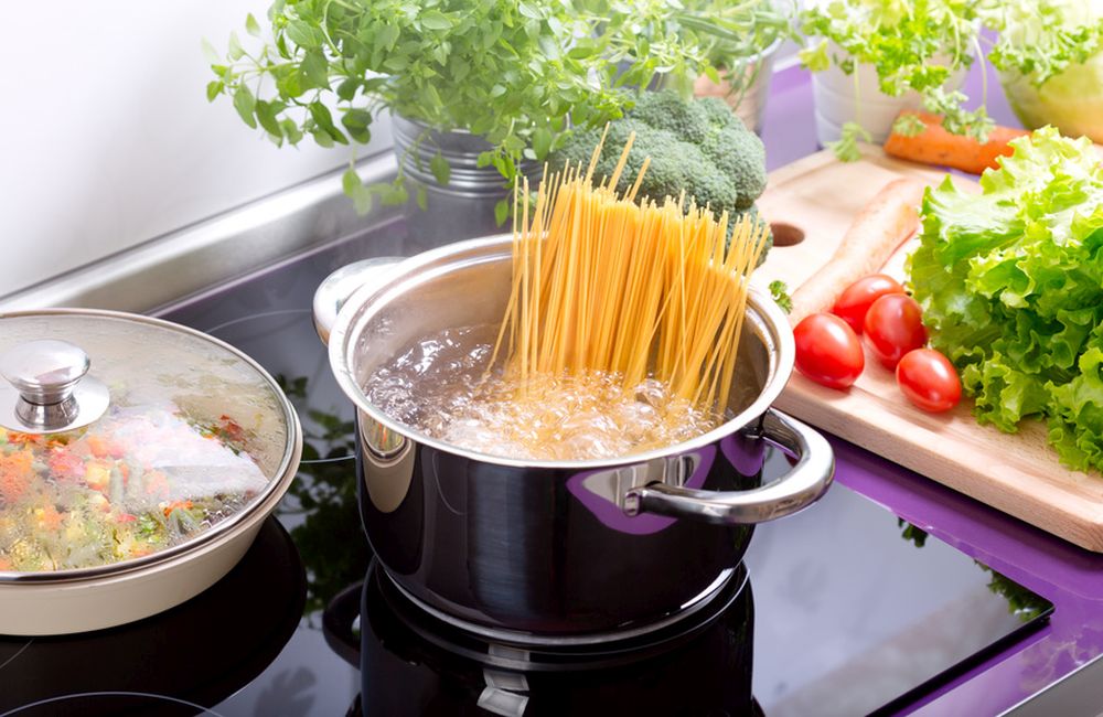 garnek z wrzącą wodą i spaghetti na kuchence w kuchni