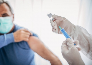 Two people, medical doctor in protective suit giving a senior male Covid-19 coronavirus vaccine.