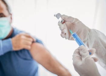 Two people, medical doctor in protective suit giving a senior male Covid-19 coronavirus vaccine.