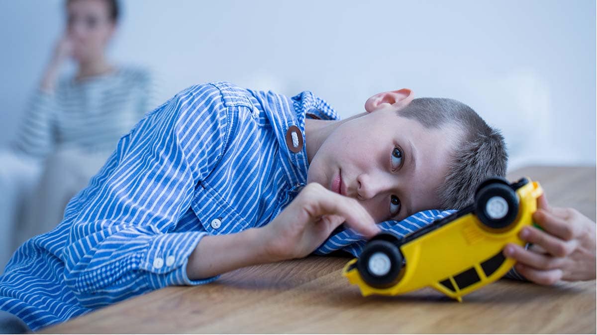 Sad autistic boy playing with toy car on wooden table