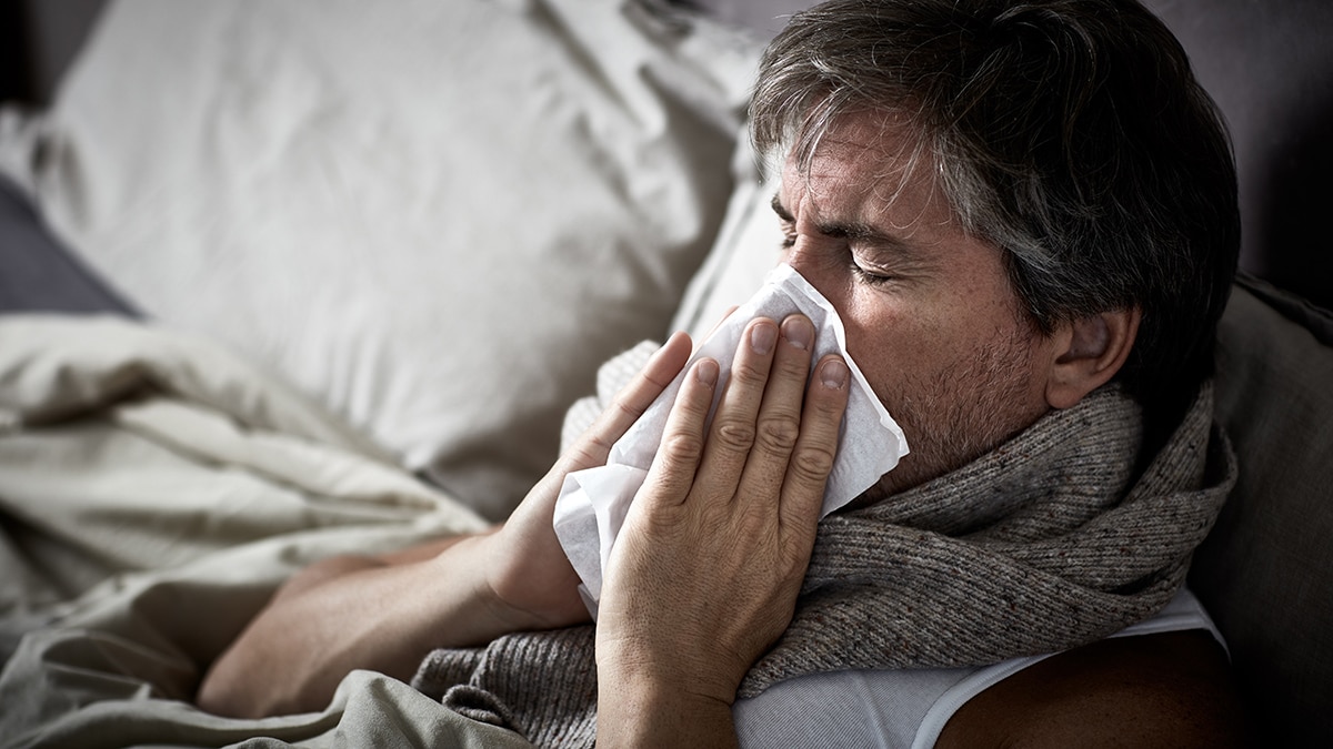 Sick man with flu lying in bed and blow nose napkin.